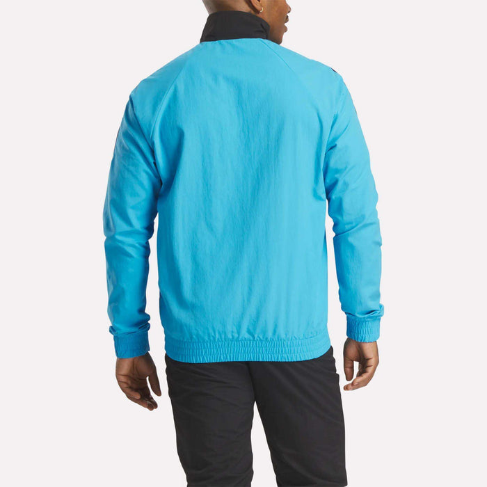 A person is shown from the back against a plain white background wearing the Reebok Men's Classics Track Top in bright blue and black pants, highlighting casual comfort.