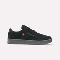 A pair of Reebok Men’s Club C 85 Shoes in Black/Grey 4, featuring a gray sole, black laces, and a subtle red Reebok logo on the side, is displayed against a plain white background. These classic sneakers offer a sleek design paired with everyday comfort.