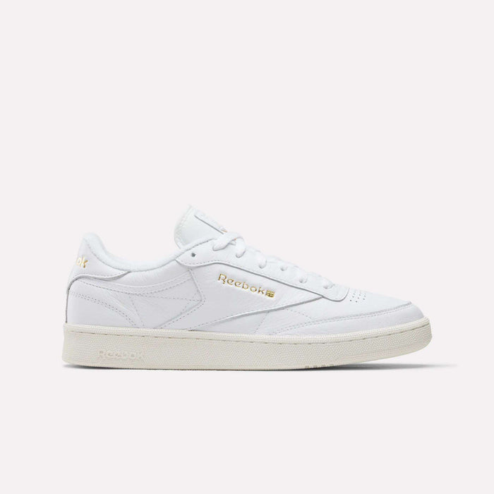 The Reebok Men's Club C 85 Shoes in Ftwr White/Chalk/Gold feature premium leather, a low-top silhouette, gold branding, white laces, and a slightly off-white sole, displayed on a plain white background.