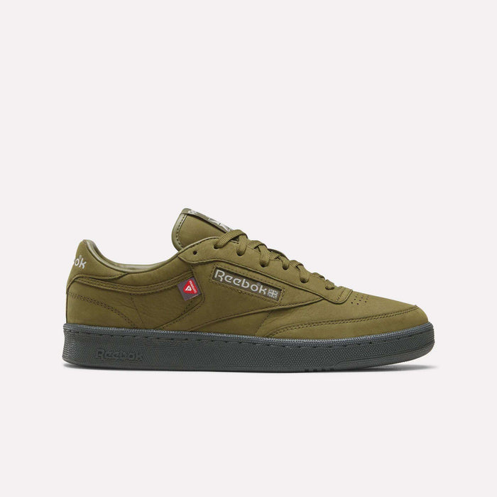 Men’s Club C 85 Shoes by Reebok in Olive Stone/New Grey 1/Grey 5 are displayed in profile on a plain white background. These stylish sneakers feature a black sole, a red accent near the laces, and a Reebok logo with Japanese text on the side.