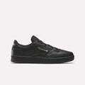 A side profile of the Men’s Club C 85 Shoes by Reebok is shown against a plain white background. This sneaker, in a Black/Almostblack/Gold colorway, is crafted from premium garment leather and features gold Reebok branding. The iconic design and elevated materials capture the timeless appeal of retro shoes.