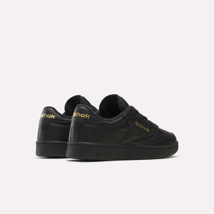 A pair of Men’s Club C 85 Shoes by Reebok in black, crafted from premium garment leather with gold Reebok branding, is displayed on a plain white background. The retro sneakers are angled to showcase both the side and back views.