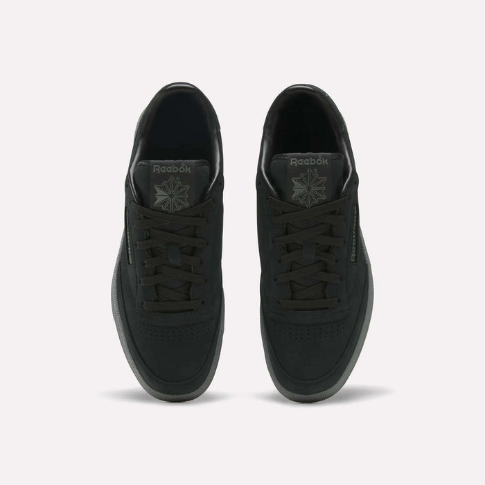 A pair of Men’s Club C 85 Shoes by Reebok in black are displayed from an overhead view, highlighting the laces, perforated toe area, branding on the tongue, and side logo against a light background.