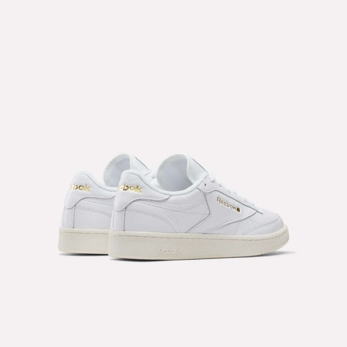 A pair of Reebok Men's Club C 85 Shoes in white garment leather with gold logo accents, white laces, and beige rubber soles—displayed angled to show side and back views against a plain light background.