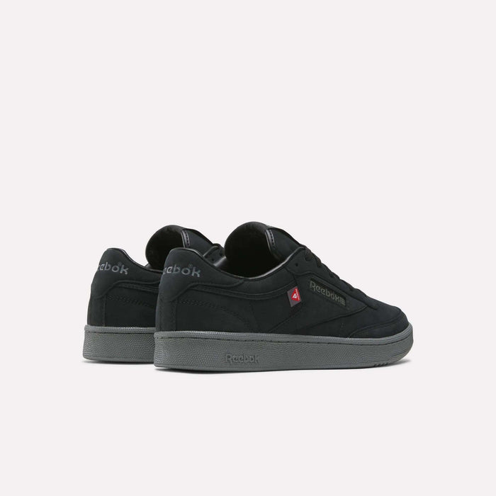 A pair of Reebok Men’s Club C 85 Shoes in black with gray soles, arranged at an angle on a plain white background. The left shoe is set slightly behind the right, displaying both the side and back views.