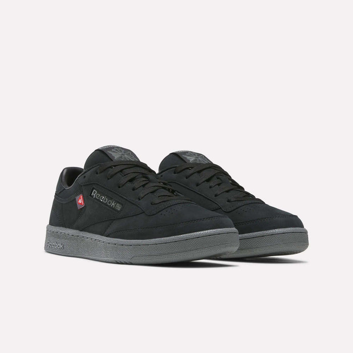 A pair of Reebok Men’s Club C 85 Shoes in black, featuring gray soles, black laces, and red logo accents on the side, displayed on a plain white background.