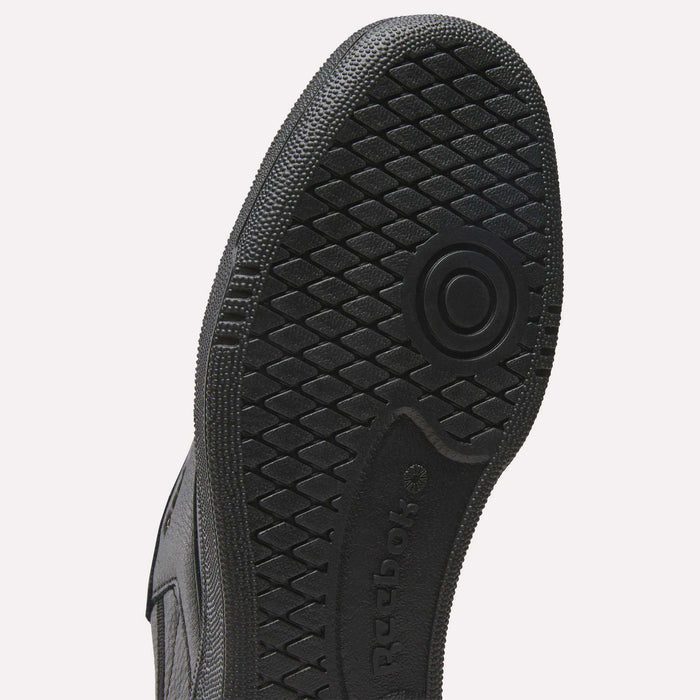 Close-up of the black rubber sole of a Reebok Men’s Club C 85 Shoe featuring a textured, diamond-shaped grip pattern and circular design, with the Reebok logo embossed on the arch area. The upper is crafted from premium garment leather, complementing its timeless silhouette.