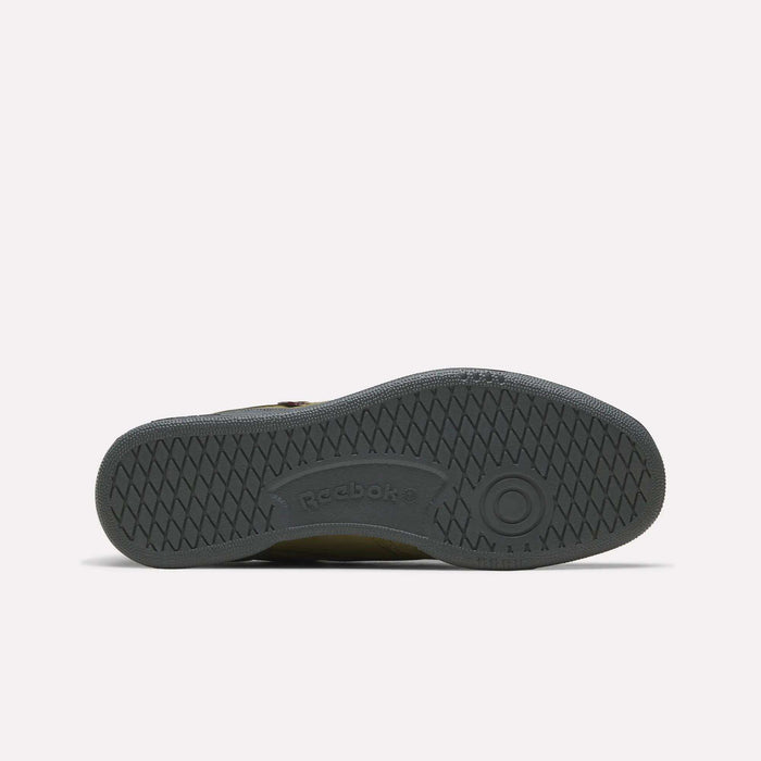 The image shows the dark gray rubber sole of a Men’s Club C 85 Shoe by Reebok lying flat with the sole facing upward. The tread pattern features textured crisscross lines and circular designs, with the Reebok® logo embossed in the center.