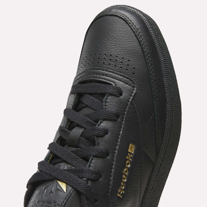 Close-up of the Reebok Men’s Club C 85 Shoes in black, showcasing premium garment leather, black laces, perforated toe, textured side panels, and gold Reebok branding on the side.