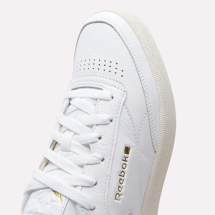 Close-up of Reebok Men's Club C 85 Shoes in white, crafted from premium leather with white laces, textured leather accents, a gold Reebok logo on the side, and a light beige sole with textured grip.