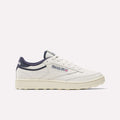 The Reebok Men's Club C Golf Shoes are white with navy blue accents, a beige spikeless outsole, and feature the Reebok logo with a small Union Jack on the side, displayed in a side profile on a plain white background.