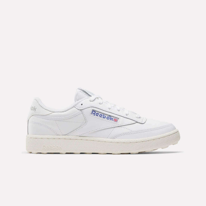 The Men's Club C Golf Shoes by Reebok are white, low-top sneakers with the Reebok logo and Union Jack on the side, water-resistant leather, white laces, and a textured off-white spikeless outsole, shown against a plain light background.
