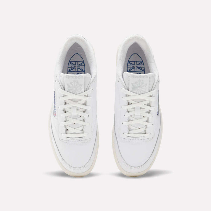 A pair of white Reebok Men's Club C Golf Shoes viewed from above, featuring water-resistant leather, white laces, a subtle beige spikeless sole, blue Reebok branding, and the Union Jack flag on each tongue.