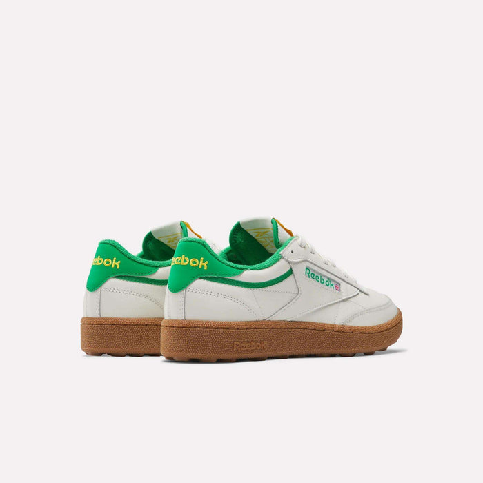 The Men's Club C Golf Shoes by Reebok feature white, water-resistant leather uppers, green accents on the heel and collar, yellow branding, and gum rubber soles with a spikeless outsole, shown from a rear-side angle on a plain white background.