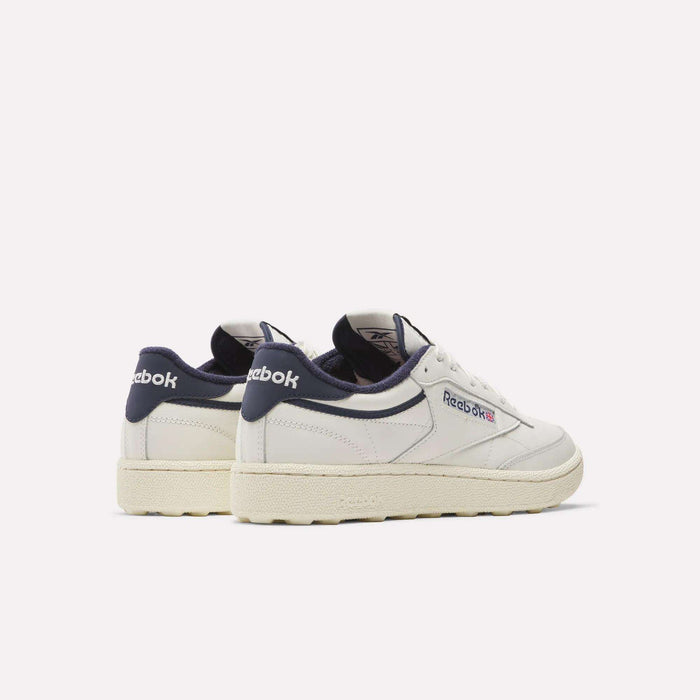 A pair of Reebok Men's Club C Golf Shoes in white with navy accents and off-white soles, featuring water-resistant leather uppers and a spikeless outsole, displayed on a plain light background, one showing the back and the other the side.