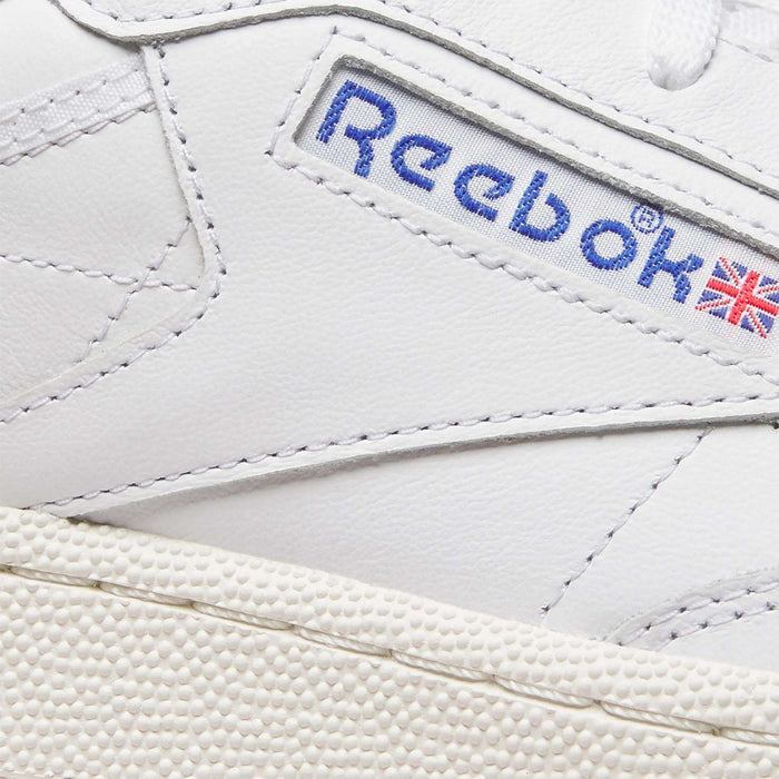 Close-up of Reebok Men's Club C Golf Shoes in white, made from water-resistant leather with stitched accents and the Reebok logo featuring a small British flag. The photo also shows part of the textured, spikeless outsole.