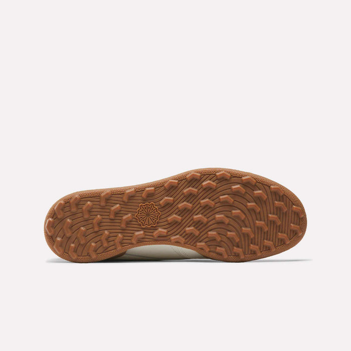 The image displays the brown rubber spikeless outsole of Reebok Men's Club C Golf Shoes, featuring a wavy tread and central geometric star-like logo, photographed against a plain white background.