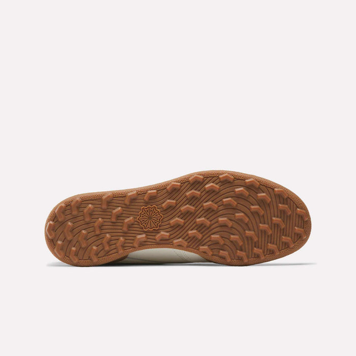The image displays the brown rubber spikeless outsole of Reebok Men's Club C Golf Shoes, featuring a wavy tread and central geometric star-like logo, photographed against a plain white background.