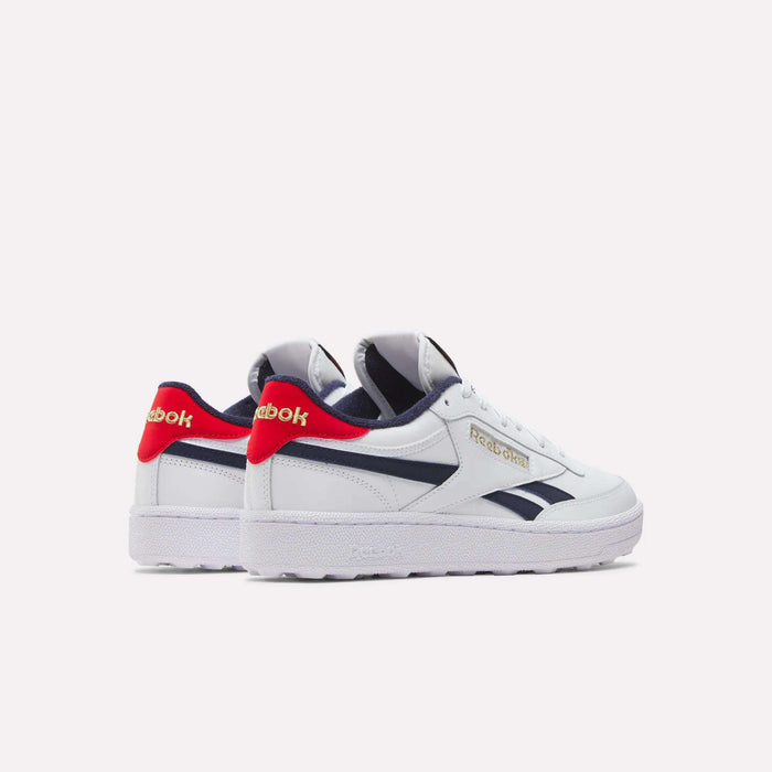 The Men's Club C Revenge Golf Shoes by Reebok feature a white design with navy blue and red accents, spikeless outsole, and Reebok logos on the sides and heels, shown against a plain white background.
