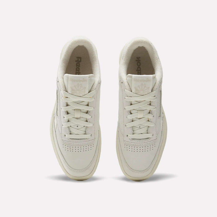 Top view of men's Reebok Club C Revenge Shoes in cream, featuring white laces, perforated nubuck leather toes, and visible Reebok logos on the tongues, set on a plain white background.