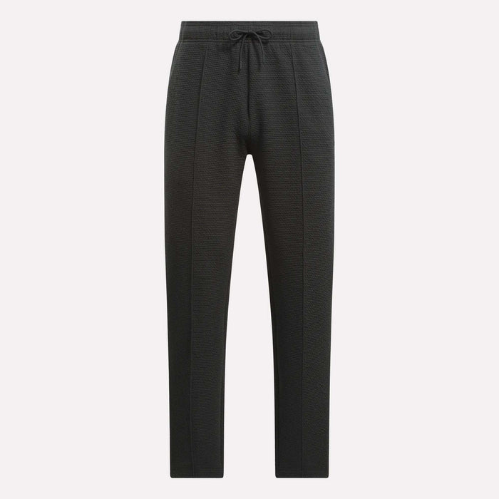 Men's Club Sport Textured Pants by Reebok feature a black textured design, slim tapered fit, and drawstring waistband with front panel seams and tapered legs, shown against a plain white background.