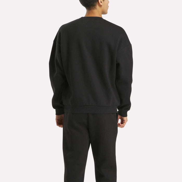 A person stands with their back to the camera wearing the Reebok Men's Cottle Sweatshirt and matching black pants against a plain light background.