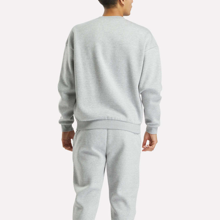 A person faces away from the camera, wearing the Reebok Men's Cottle Sweatshirt in light gray, styled with matching sweatpants, set against a plain white background.