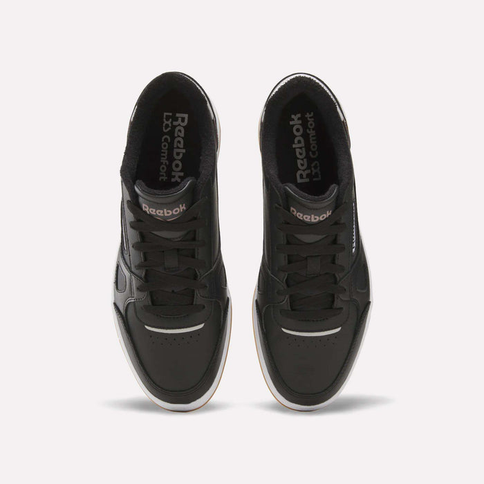 A pair of Reebok Men’s Court LXS Shoes in black, made from full grain leather, are shown from above with visible laces, perforated toe boxes, and Reebok branding on the tongues. The shoes feature white midsoles and are positioned side by side on a plain background.