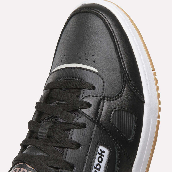 A detailed close-up of the Reebok Men’s Court LXS Shoes in black, showcasing black laces, a crisp white midsole, and a distinctive gum outsole. Made from premium full grain leather, these men’s court shoes feature the iconic Reebok logo on the side.