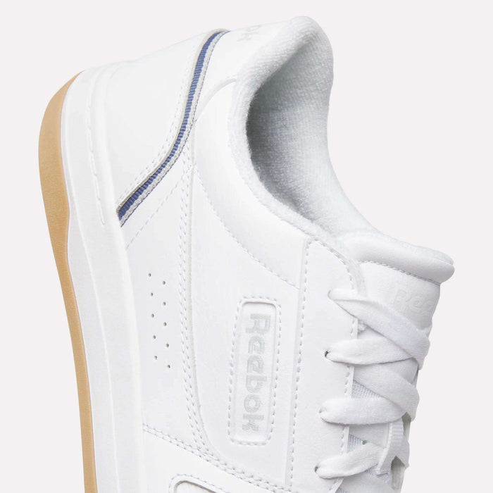 A close-up of the Men’s Court LXS Shoes by Reebok showcases white laces, a light brown sole, and a blue accent near the heel. Crafted from premium full grain leather, these shoes are set against a plain background.
