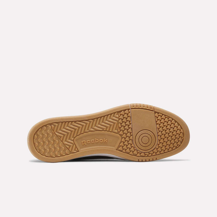 The image features the brown rubber outsole of the Reebok Men’s Court LXS Shoes, highlighting multiple tread patterns and the Reebok logo near the arch. Crafted as men’s court sneakers, this style complements its outsole with a premium full grain leather upper.