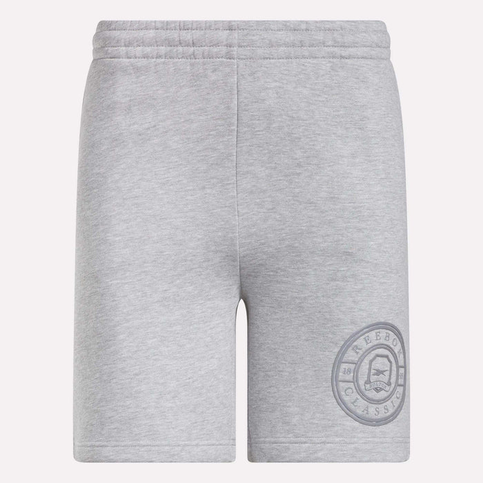Reebok Men's Crest Shorts in light grey feature an elastic waistband and relaxed fit. Made from cotton, these shorts have a simple design without visible pockets or drawstrings and display a circular Reebok Classic logo on the lower left leg.