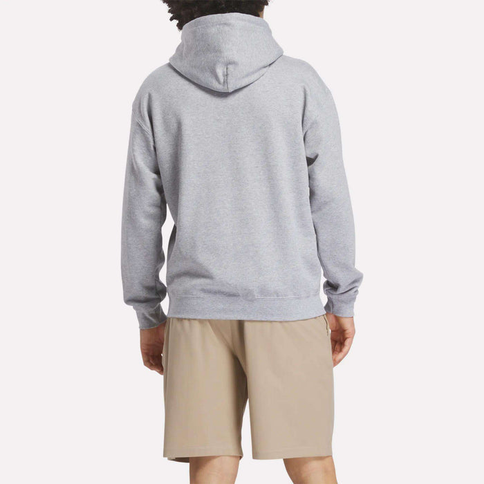 A person faces away from the camera, wearing a light gray Reebok Men's Crushers Hoodie and beige shorts against a plain, light background.