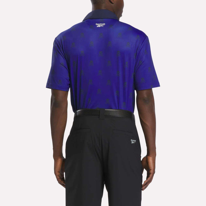 A man is shown from the back wearing a deep blue Reebok Men's Crushers Polo Shirt with short sleeves and black pants. The performance golf polo shirt features a subtle pattern and a logo near the collar, highlighting classic golf style; the pants also display a small logo on the right pocket area.
