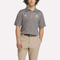 A person wears a gray Reebok Men's Crushers Replica Polo with embroidered logos and light khaki pants, standing with one hand in their pocket against a plain white background.