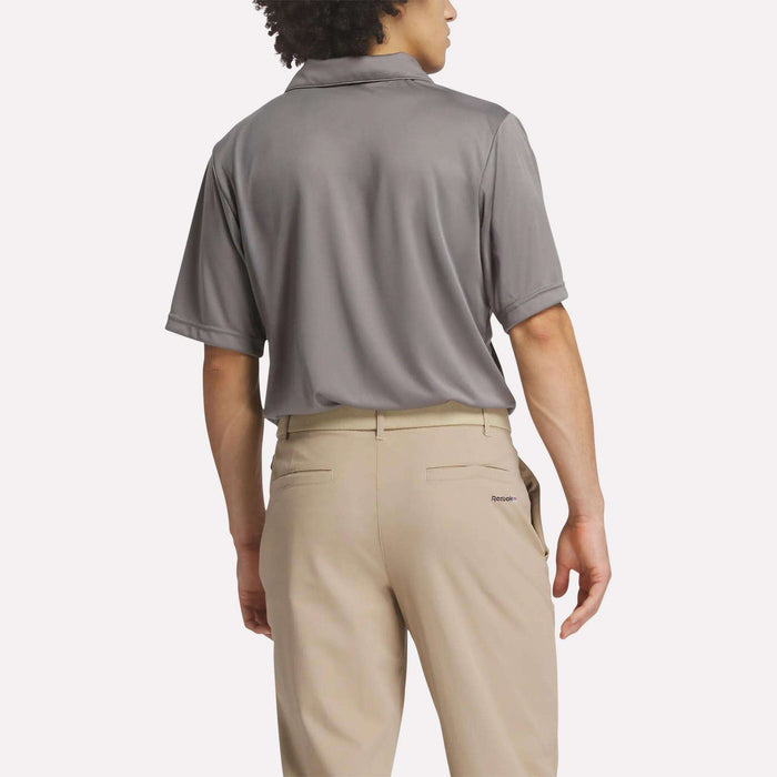A person is shown from the back, wearing a gray Reebok Men's Crushers Replica Polo with short sleeves and beige pants featuring belt loops and welt pockets, standing against a plain light background.