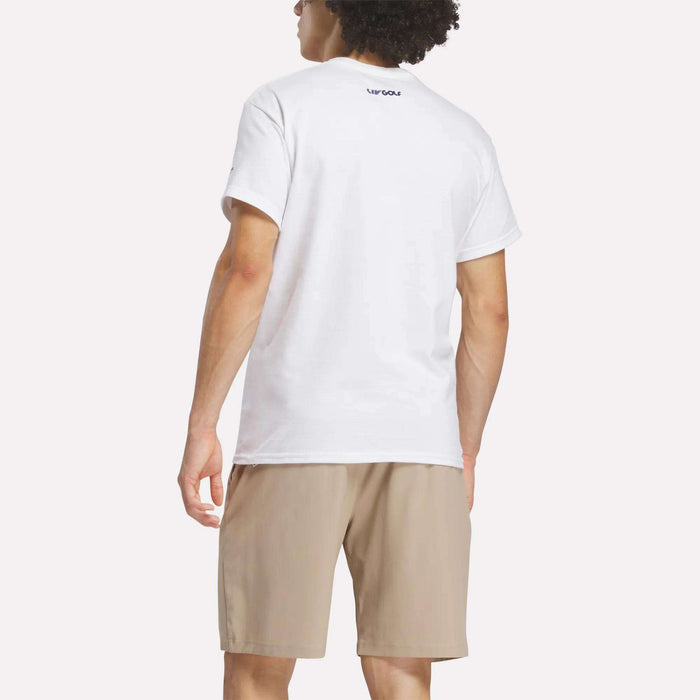 A person with curly hair is shown from the back, wearing a white Reebok Men's Crushers Stacked Logo Tee and beige shorts, standing against a plain light background.