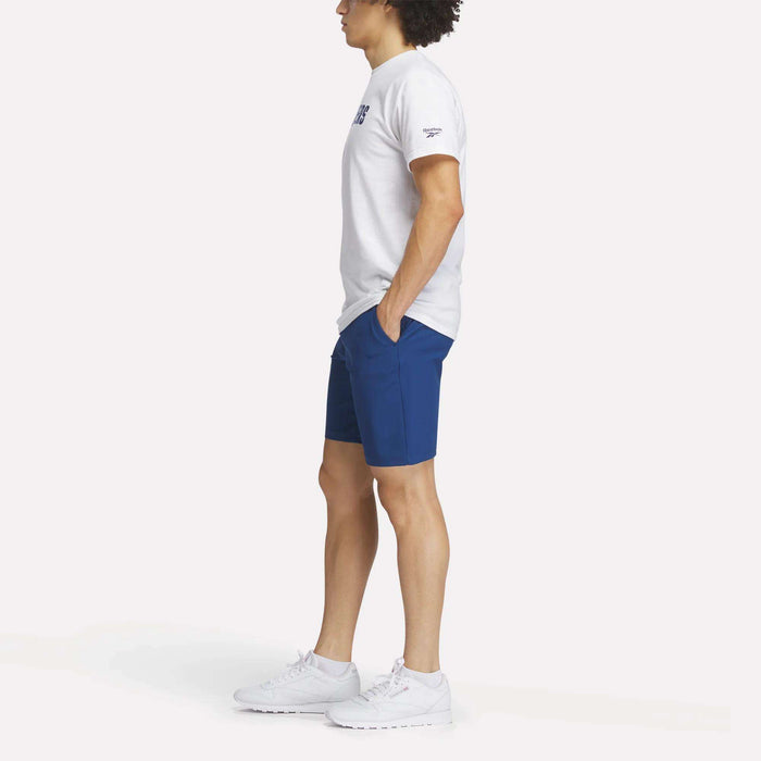 A man in shorts and a white Reebok Men's Crushers Wordmark Tee.