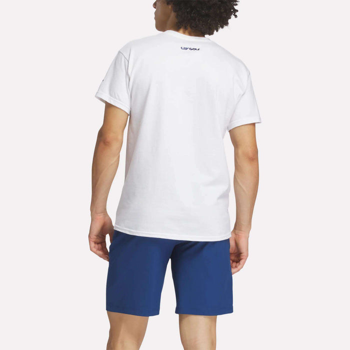 A person with curly hair is shown from the back wearing a plain white Reebok Men's Crushers Wordmark Tee and blue shorts. The background is bright and uncluttered. The word REEBOK is printed on the upper back of the T-shirt.