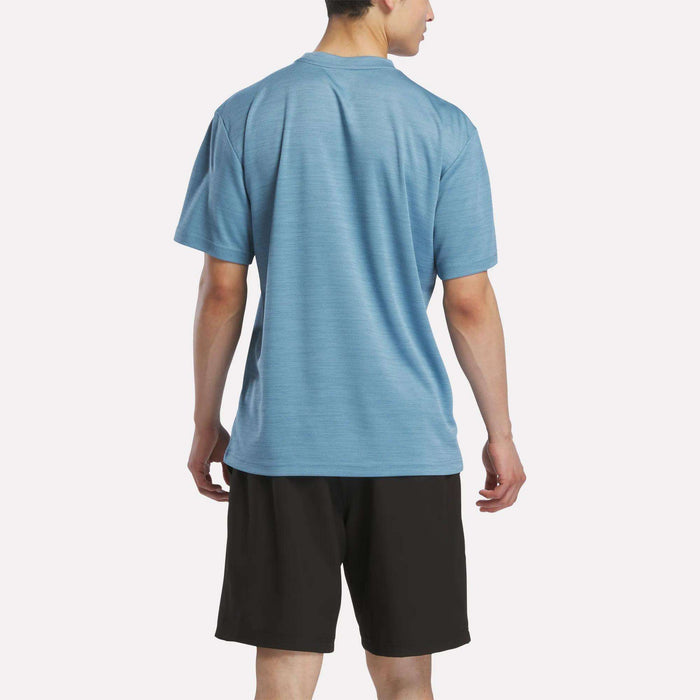 A man wearing a Reebok Men's Director Short Sleeve Top and black shorts stands with his back to the camera against a plain white background.