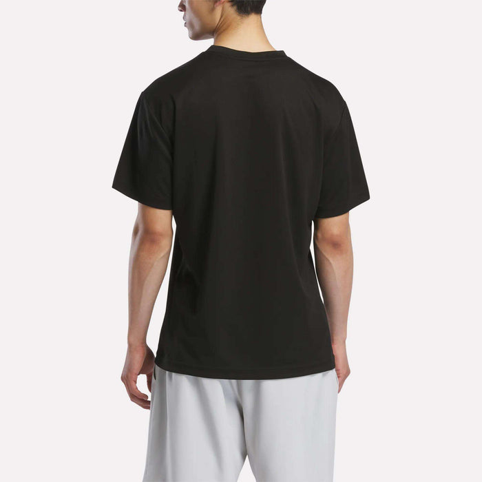 A person stands with their back to the camera, wearing the Reebok Men's Director Short Sleeve Top and light-colored shorts against a light background.