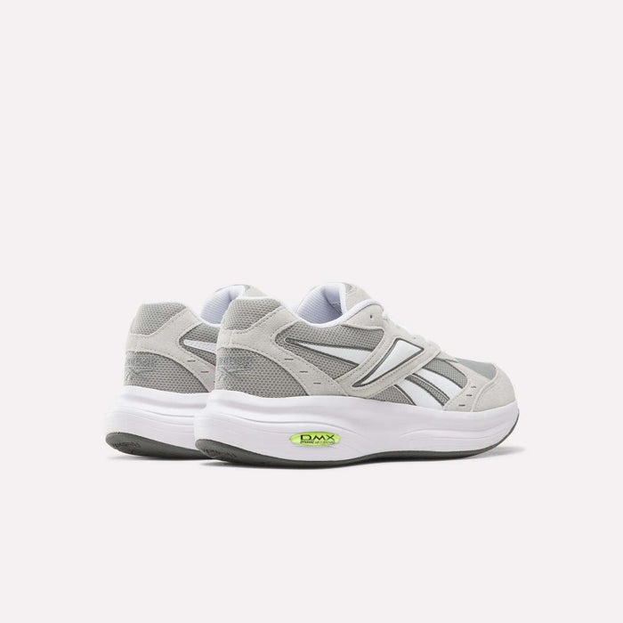 A pair of Reebok Men’s DMX Comfort+ Walk Ultra Shoes in gray and white, featuring green DMX Comfort+ cushioning visible in the soles, are displayed on a light background and angled to highlight the backs and sides of these athletic walking sneakers.