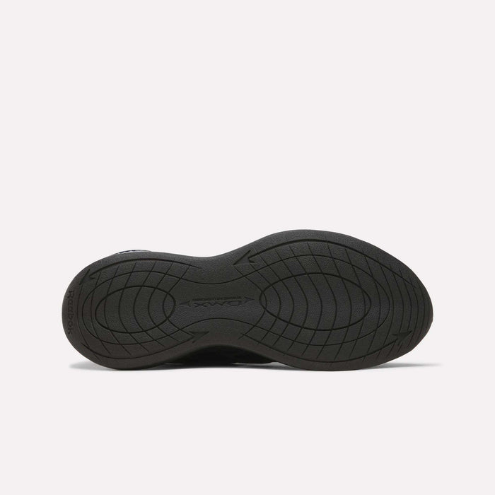 The image displays the black rubber sole of a Reebok Men’s DMX Comfort+ Walk Ultra Shoe, featuring curved grooves and traction patterns, photographed against a plain white background.