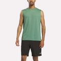 A man wearing a Reebok Men's Elite Sleeveless Top in Field Green Heather stands facing forward against a plain white background, paired with black athletic shorts.
