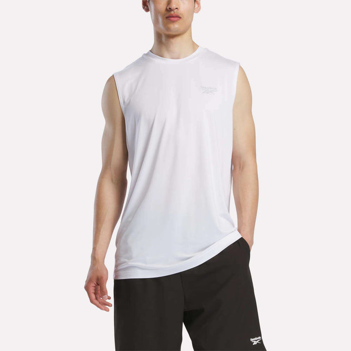 A man wears a Reebok Men's Elite Sleeveless Top in white cotton flex knit and black shorts, standing with one hand in his pocket against a plain background.