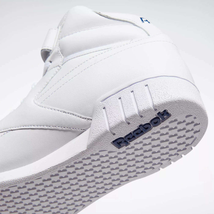 Close-up of the Men's EX-O-FIT Hi Shoes by Reebok shows the white leather upper, textured sole, and side panel with an embossed blue Reebok logo. Tilted to highlight its clean retro design and grippy outsole pattern.