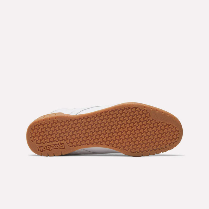 The image shows the sole of Reebok Men's EX-O-FIT Hi Shoes, featuring a brown rubber outsole with a textured grip pattern and embossed Reebok logo near the heel. The partially visible white upper adds to its retro style.