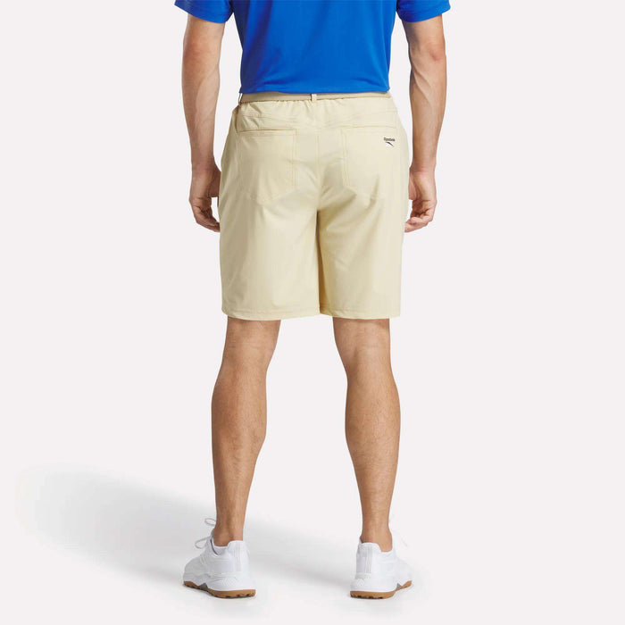 A man stands facing away against a plain white background, wearing a blue polo shirt, white sneakers, and Reebok Men's Favorite 5-Pocket Golf Shorts 9".