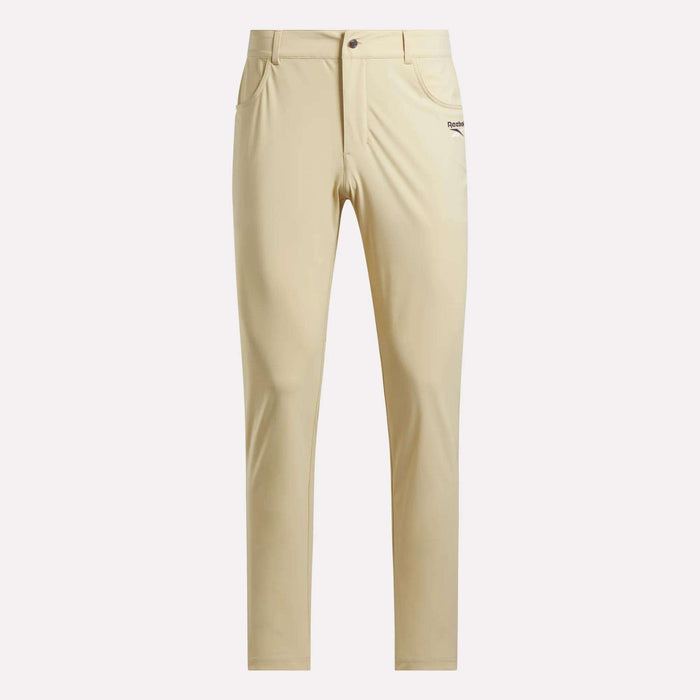 Men's Favorite 5-Pocket Relaxed Fit Golf Pants by Reebok in beige, featuring RBK-DRY tech, front pockets, button and zip closure, wrinkle-resistant fabric, and a small logo by the pocket—shown on a plain light background.