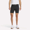 A man models Reebok Men's Favorite Golf Shorts 8.5", paired with a white polo, black belt, and white sneakers against a plain white background; only his body from the shoulders down is shown.